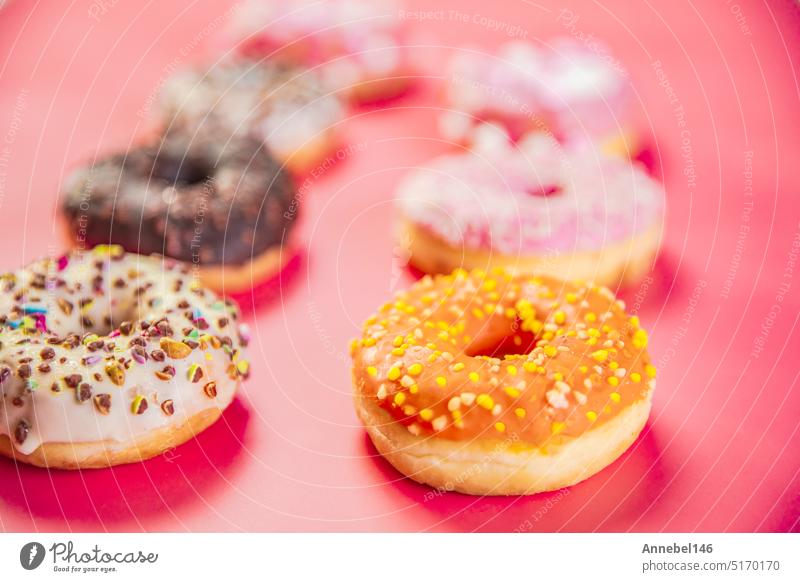 Krapfen mit mehrfarbiger Glasur in zwei Reihen auf trendigem rosa Hintergrund. Doughnuts sind ein traditionelles süßes Gebäck. Platz zum Kopieren von Text.