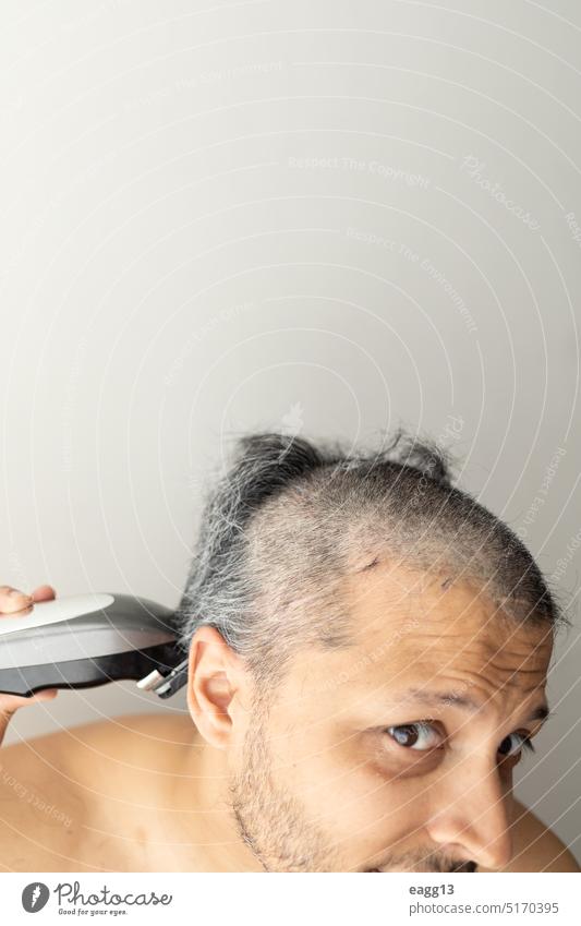 Ein stattlicher grauhaariger Mann schneidet sich selbst die Haare. Erwachsener zu Hause Bad Vollbart Körper Pflege Schermaschine abschließen geschnitten