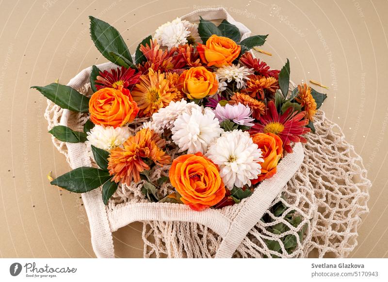 Orange und rote Gartenblumen in der Netztasche Mockup weißen Tags mit Platz für Text Hintergrund in natürlichen Erdtönen Rosen, Gänseblümchen, Chrysanthemen