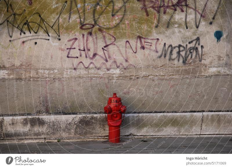 Eine knallrote Wasserzapfstelle für die Feuerwehr vor einer alten mit Graffiti bemalten Hauswand Graffiti-Wand graffity wasserspender Amatur Amaturen feuerrot