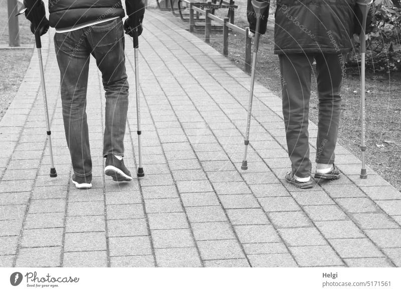 Rückansicht zweier Männer, die mit Unterarmgehstützen laufen Mensch Mann Senior Teilansicht Beine Stützen gehen Park Weg Kurort Übung Krankheit Erholung Reha