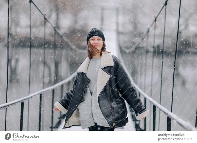 Eine Frau geht über den Fluss auf einer Hängebrücke im Winter Tag. Junges Mädchen in warmer Kleidung steht auf einer hölzernen Fußgängerbrücke in kalten verschneiten Tag