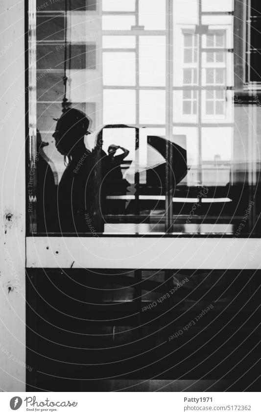 Menschliche Silhouetten vor einer geometrischen Fassade reflektieren in einer Glasscheibe Spiegelung mann mit hut Schatten geheimnisvoll Reflexion & Spiegelung