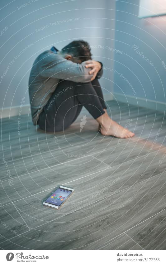 Mann mit Problemen auf dem Boden sitzend mit Handy auf dem Boden unkenntlich gesichtslos Typ verzweifelt Problematik Deckung Gesicht mental Erkrankung Sitzen
