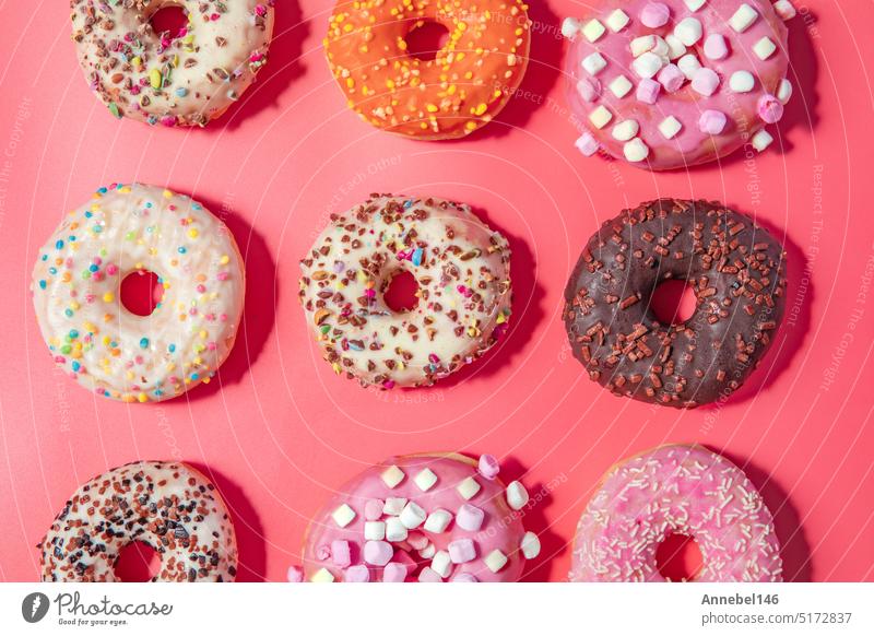 Donuts mit Zuckerguss auf pastellrosa Hintergrund. Süße Donuts. Draufsicht sortiert mit verschiedenen Schokolade glasiert und Streusel, Zucker Süßigkeiten Konzept