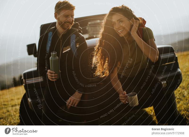 Junges Paar entspannt sich auf der Motorhaube eines Geländewagens auf dem Lande Erwachsener Abenteuer attraktiv Auto Automobil Mann Pause Windstille PKW