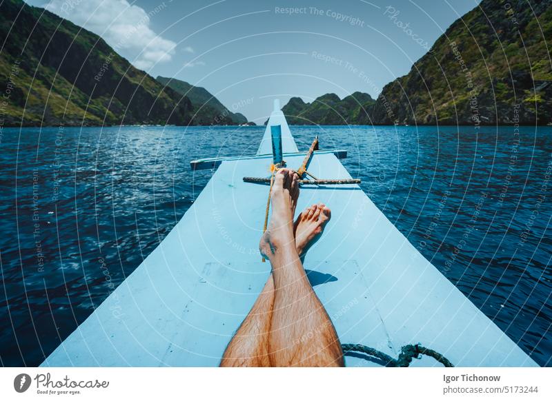 Beine eines Mannes auf einem Banca-Boot, das sich einer tropischen Insel nähert. Reise-, Entspannungs- und Urlaubskonzept Erholung Freiheit reisen Wasser Tag