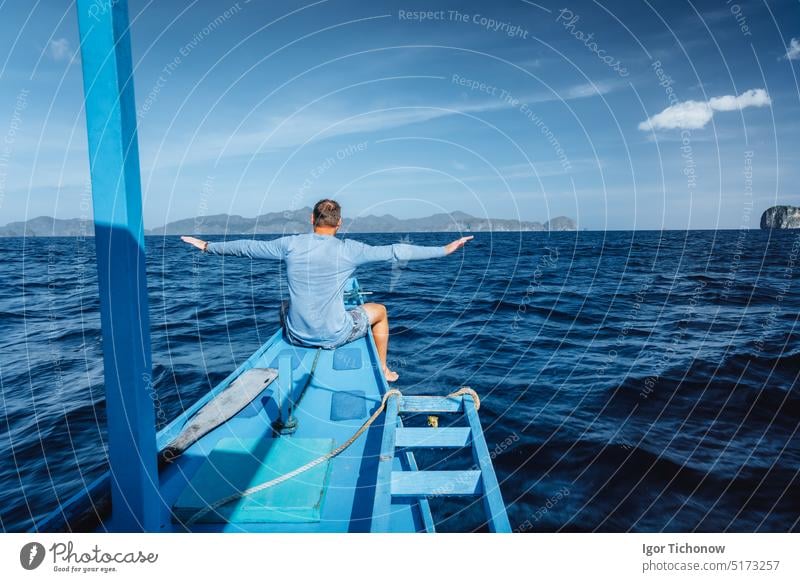Rückansicht eines Mannes auf einem Boot mit ausgebreiteten Händen, der auf einer exotischen tropischen Insel ankommt, die von der Sonne beleuchtet wird. Reisetour in Asien: El Nido, Palawan, Philippinen