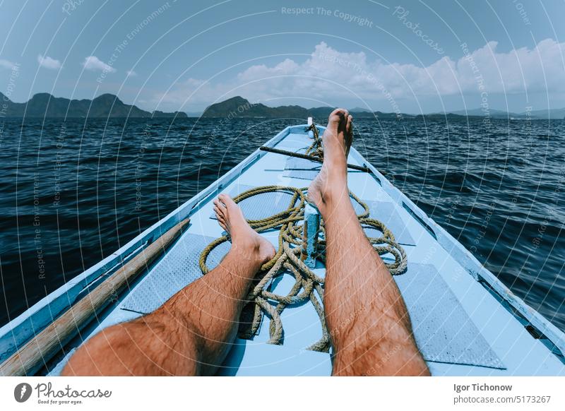 Beine des Mannes auf Banca Boot nähert sich tropischen Insel. Reise, Sommer exotischen Urlaub Urlaub Konzept Tourist Erholung persönliche Perspektive Glück