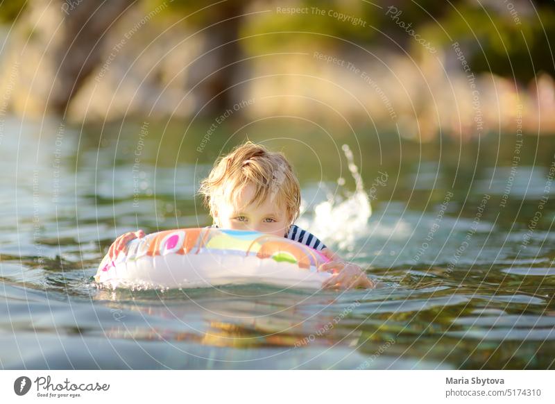 Kleiner Junge schwimmen mit bunten schwimmenden Ring im Meer auf sonnigen Sommertag. Nettes Kind spielt in sauberem Wasser. Familie und Kinder Resort Urlaub während der Sommerferien.