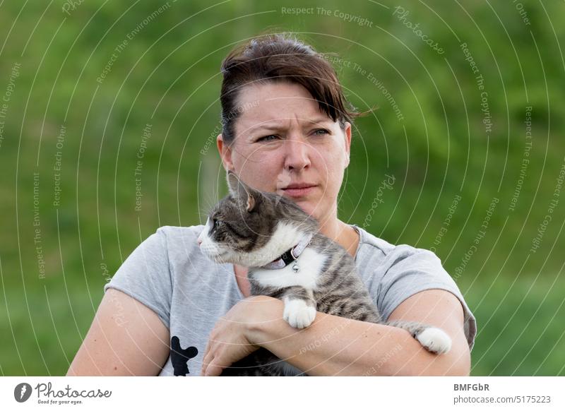 Frau hält Katze auf dem Arm. Frau schaut kritisch nach rechts, Katze kritisch nach links. halten Armen blicken unterschiedliche Richtungen lustig goldig grün