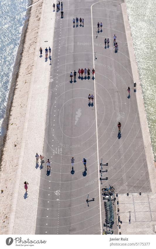 Luftaufnahme von Gruppen von Menschen in der Ferne, die an einem Sommertag eine von Kanälen mit Wasser umgebene Fußgängerzone entlangschlendern, einige Motorroller sind auf der Straße geparkt
