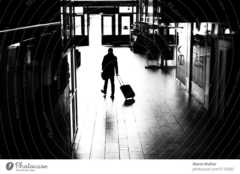Eine Silhouette von einem Mann mit Rollkoffer in einer Bahnhofshalle Schwarzweißfoto Koffer rollkoffer reisen allein Licht Mensch Gepäck Reisender