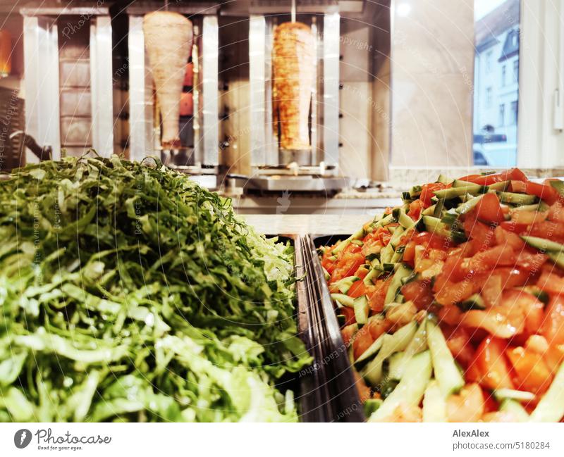 Grüner Salat und Tomaten-Gurkensalat vor zwei Dönerspießes in einem Imbiss Imbiß Essen Fleisch Kalbsfleisch Hähnchenfleisch Geflügel essen gehen auswärts