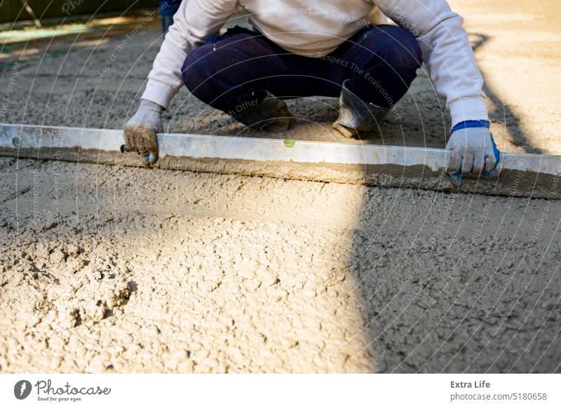 Arbeiter nivelliert frischen Beton nach dem Gießen Ausrichten Basis Bauherr Baustelle Zement Tiefbau betonieren Konstruktion Entzerrung Gleicht  aus. Entspricht