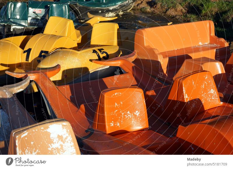 Alte Tretboote aus Kunststoff in leuchtendem Gelb und Orange im Delphin Design am Bootssteg im Sommer im Licht der Abendsonne am Poyrazlar Gölü bei Adapazari in der Provinz Sakarya in der Türkei