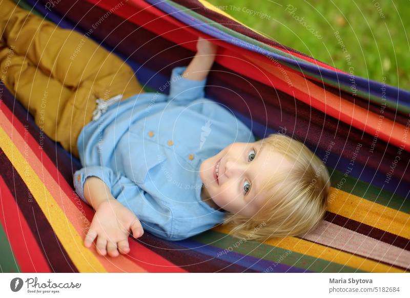 Nette kleine blonde weiße Junge genießen und Spaß haben mit bunten Hängematte im Hinterhof oder Spielplatz im Freien. Sommer im Freien aktive Freizeit für Kinder. Kind entspannt und schwingt in der Hängematte.