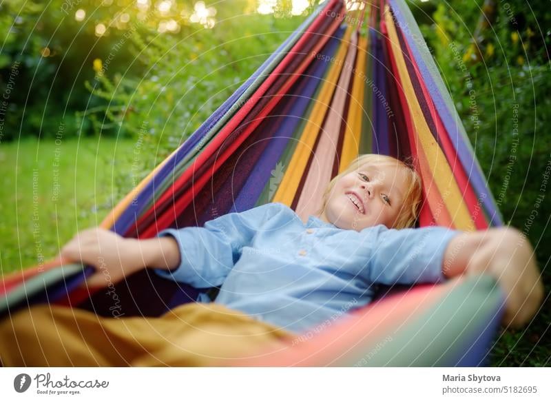 Nette kleine blonde weiße Junge genießen und Spaß haben mit bunten Hängematte im Hinterhof oder Spielplatz im Freien. Sommer im Freien aktive Freizeit für Kinder. Kind entspannt und schwingt in der Hängematte.