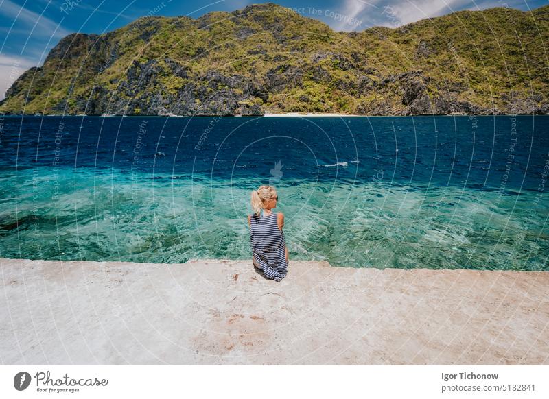 Touristin, weiblich, Rückansicht, sitzend auf der Pier-Kante der Insel Matinloc bei einer Hopfen-Tour C. El Nido, Palawan, Philippinen palawan türkis tropisch
