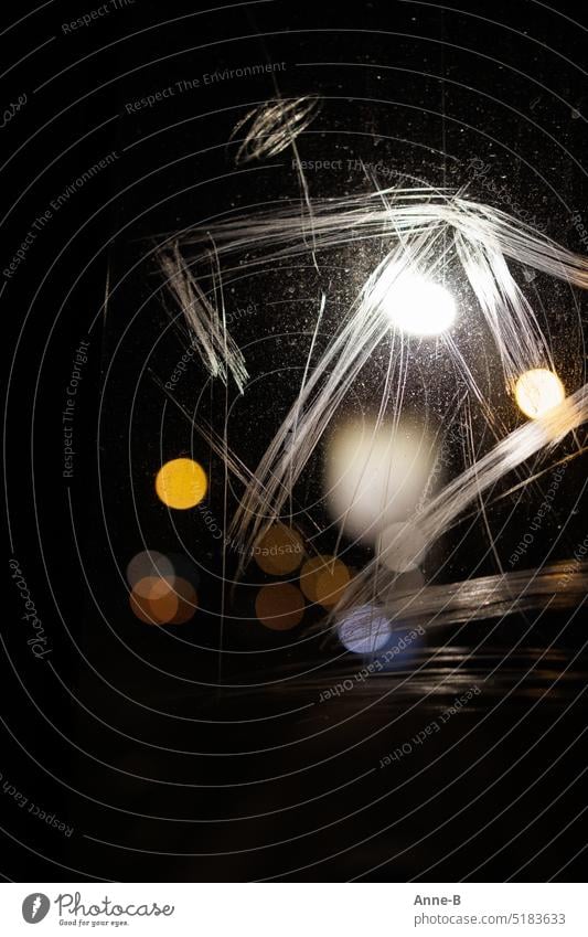 Straßenlichter als runde Punkte durch die zerkratzte Scheibe einer Haltestelle fotografiert , nachts bei Regen. Der Focus liegt auf der Scheibe.. dunkel Stadt