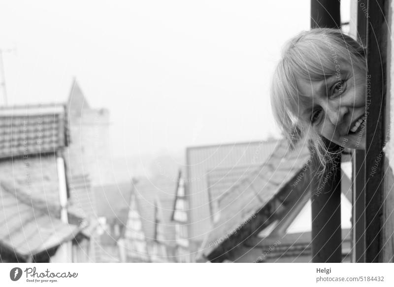 Gesicht einer lächelnden Frau, die über den Dächern einer historischen Stadt aus dem Fenster schaut Mensch Kopf Haare Lächeln Ausblick Altstadt Gebäude