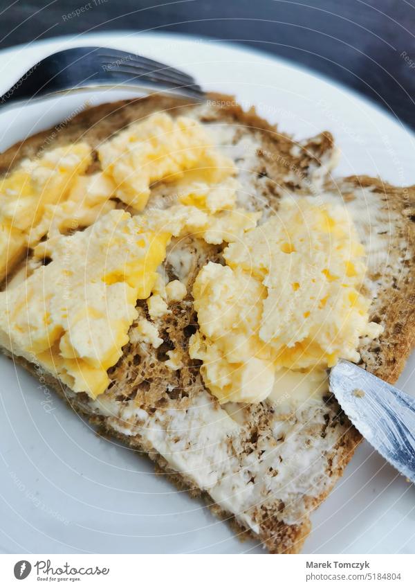 Butterbrot mit Rühreiern auf einem Teller mit Messer und Gabel. Frühstück Speise Farbfoto Brotbelag Brotscheibe Nahaufnahme Lebensmittel Essen Ei gelb Mahlzeit