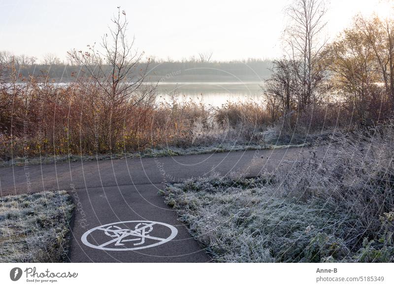 Landschaft mit See kurz nach Sonnenaufgang bei Rauhreif  mit einem asphaltiertem Weg, auf dem das Radfahren verboten ist. Rad fahren verboten Fahrrad Radfahrt