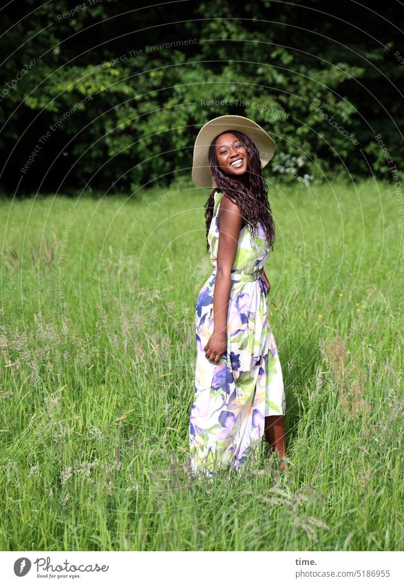 lachende Frau mit Strohhut in einer Wiese feminin Park Kleid Hut langhaarig dunkelhaarig stehen Freude Glück schön Fröhlichkeit frei Lebensfreude Begeisterung
