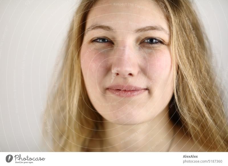 Sehr nahes Portrait einer jungen, blonden Frau, die lächelnd vor einem weißen Hintergrund steht frisch Blick in die Kamera Erwartung drinnen Selbstbewußt