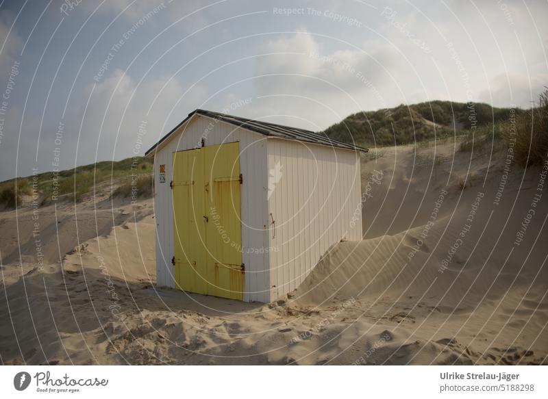 Strandhütte mit gelber Tür an Dünen von Sand umgeben Holzhütte weiße Strandhütte gelbe Holztür Sandstrand umweht verweht Hütte Sanddünen eingegraben