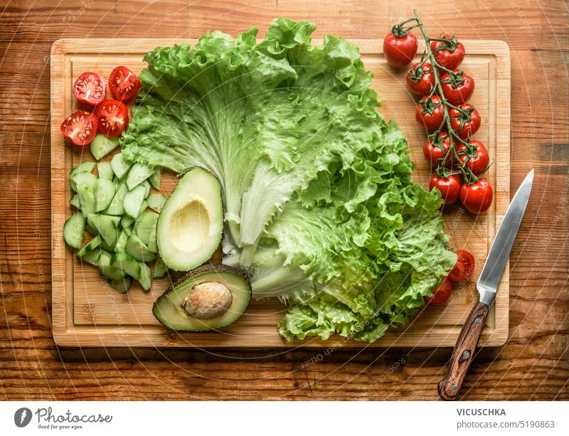 Gesunde, frische Salatzutaten: Kopfsalat, halbierte Avocado, Gurke und Tomaten auf einem Holzbrett mit Messer, Ansicht von oben Gesundheit Salatgurke hölzern