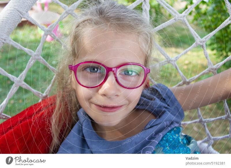 Glückliches lustiges Mädchen mit Brille Nahaufnahme in der Natur Lächeln Behaarung Kaukasier horizontal Fröhlichkeit Kind Hängesessel Straße Sommer bezaubernd