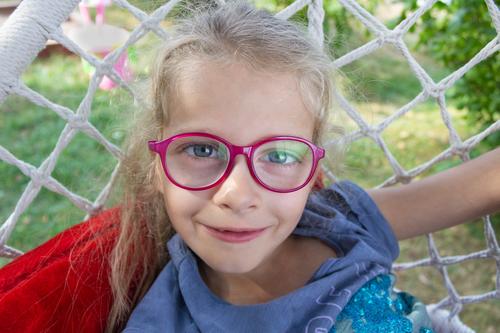 Glückliches lustiges Mädchen mit Brille Nahaufnahme in der Natur Lächeln Behaarung Kaukasier horizontal Fröhlichkeit Kind Hängesessel Straße Sommer bezaubernd