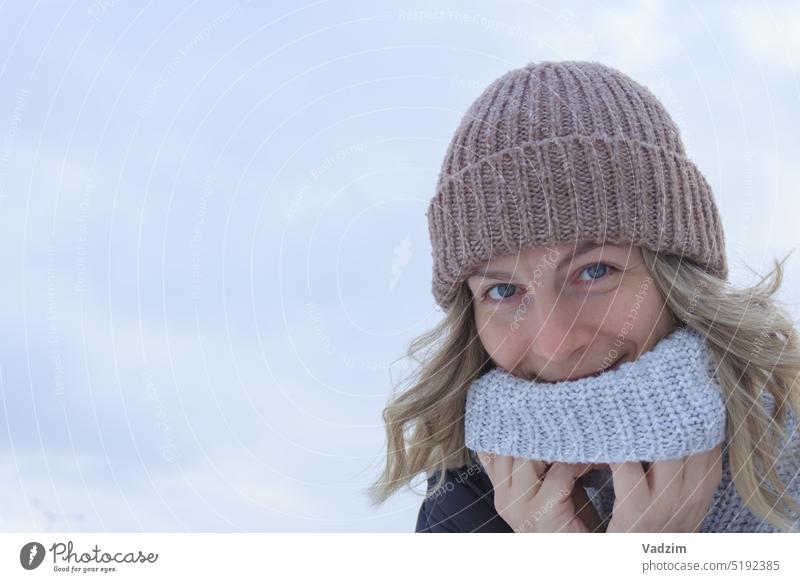Frau mit blondem Haar in Strickmütze und Pullover lächelnd auf hellem Hintergrund Nahaufnahme Gesicht Lächeln Behaarung im Freien Winter Hut gestrickt