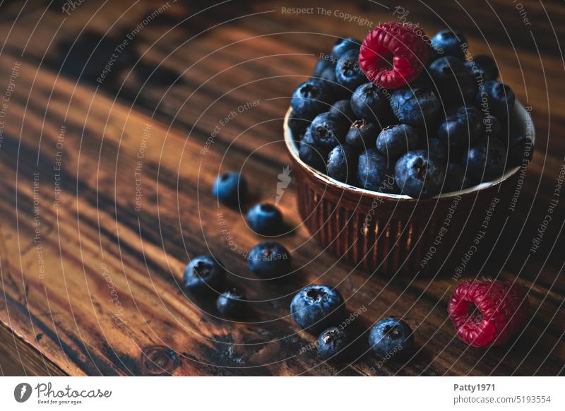 Blaubeeren und Himbeeren in einer kleinen Schale auf einem dunklen, rustikalen Holzuntergrund Foodfotografie Obst Ernährung Lebensmittel lecker