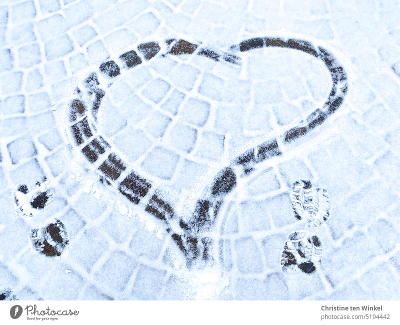 Ein gemaltes Herz und zwei Schuhabdrücke auf leicht verschneitem Kopfsteinpflaster verschneites Kopfsteinpflaster Winter Herz im Schnee Liebeserklärung