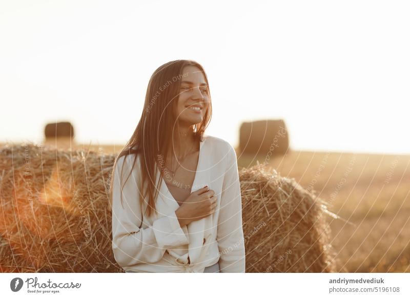Porträt eines lächelnden schönen Mädchens mit langen Haaren in einem Jeansrock. Frau, die einen Spaziergang in einem Weizenfeld mit Heuballen an einem sonnigen Sommertag genießt.
