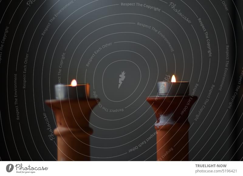 Besinnungspause mit zwei brennenden Teelichtern auf Terrakotta Leuchtern vor dunklem Hintergrund Kerzenhalter Kerzenständer leuchten Pause Stille Ruhe einfach