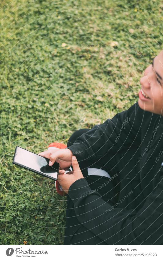 Lächelnder lateinamerikanischer Teenager, der auf seinen Smartphone-Bildschirm schaut authentisch Junge hell Browsen lässig plaudernd Mitteilung Anschluss