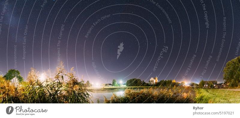 Panorama der Verdunstung über Fluss See in der Nähe von Häusern im Dorf. Nacht Sternenhimmel über See Fluss mit hellen Sternen und Meteoric Track Trail. Glühende Sterne über Sommer Natur