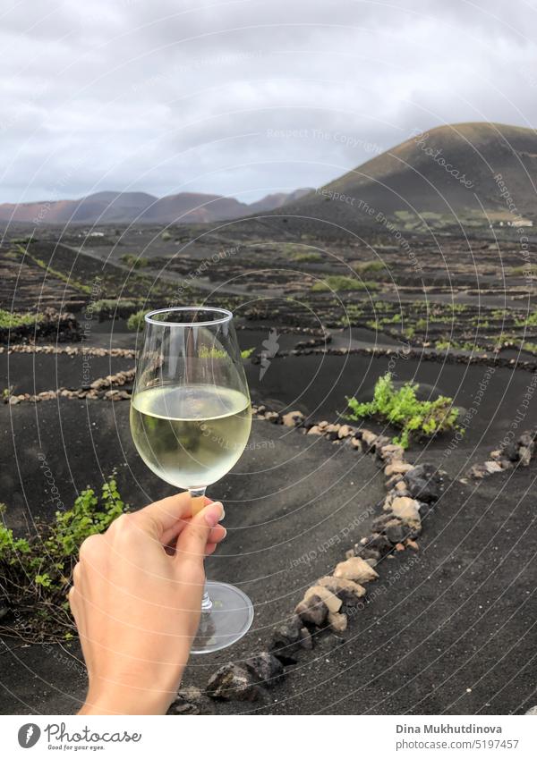 Frau hält ein Glas Weißwein auf einem Weingut in Lanzarote, Spanien. Vulkanischer Wein - Weinberg in der Nähe eines erloschenen Vulkans. Tourist reisen schön