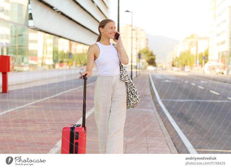 junge schöne Frau mit roten Koffer Aufruf Smartphone während des Wartens auf ein Taxi in der Stadt. stilvolle lächelnde Mädchen Tourist auf Sommerurlaub Urlaub. neue Reise. Kopie Raum