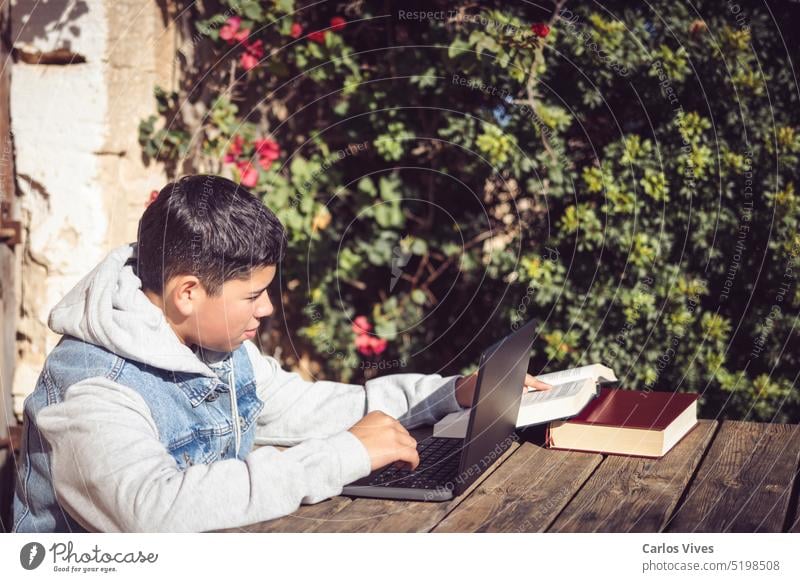 junger lateinamerikanischer Mann liest ein Buch vor einem Laptop, im Freien Bücher Bücherregal Junge zentriert Nahaufnahme Mitteilung Computer konzentriert