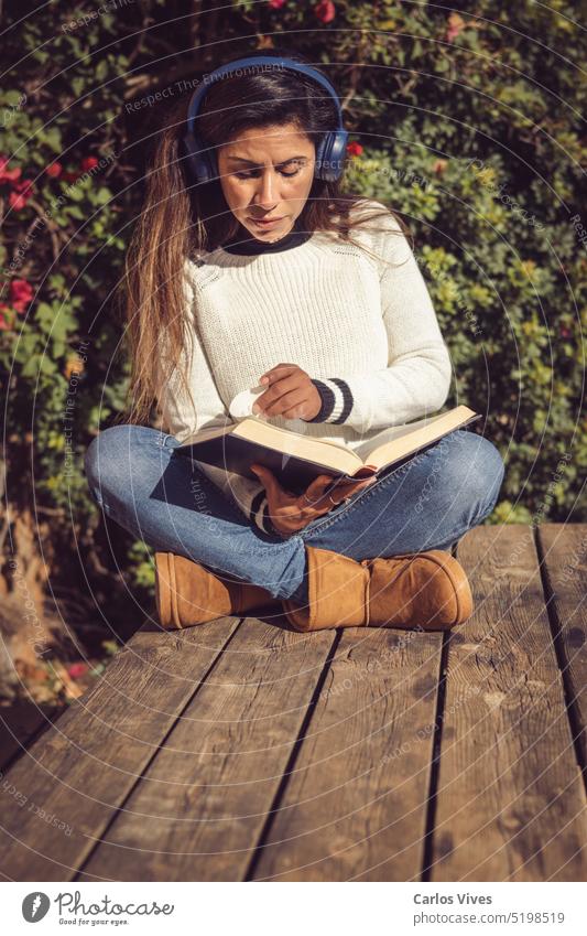 lateinamerikanische Frau, die im Freien sitzt, Musik hört und liest 40s 50s lateinamerikanerin allein schön Bestseller Komfort bequem Konzepte Textfreiraum