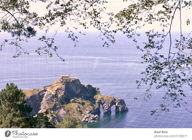 Einsiedelei von San Juan de Gaztelugatxe an einem sonnigen Tag. ruhige See, Felsformation, Löcher, Rahmen aus Ästen und Bäumen Sonnenlicht Insel Meer Ferien