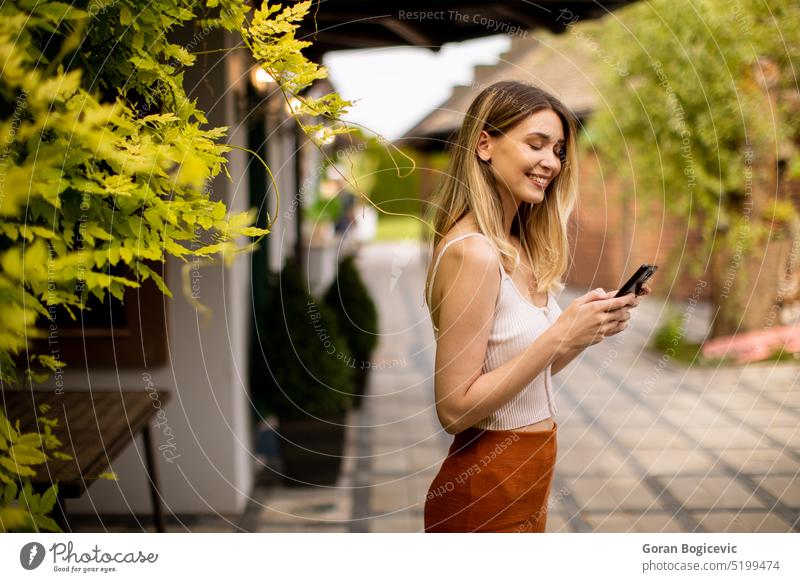 Eine junge Frau benutzt ihr Mobiltelefon an einem schönen Sommertag in einem Garten Handy Landschaft Abgelenkt Technik & Technologie lässig entspannt Natur grün