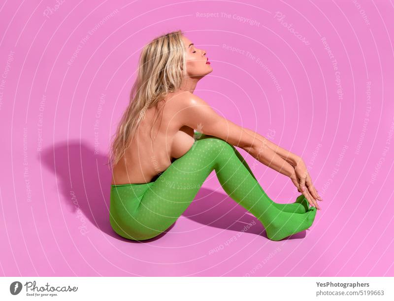 Fit Frau mit langen blonden Haaren, in grünen Strumpfhosen und oben ohne, minimalistisch auf einem lila Hintergrund Alterung sportlich schön Körper hell