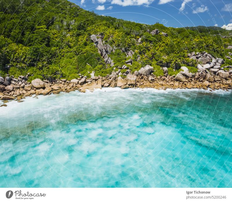 Luftaufnahme einer Drohne von einem paradiesischen Strand mit kristallklarem, türkisfarbenem Wasser, bizarren Granitfelsen und Kokosnusspalmen. Reisekonzept