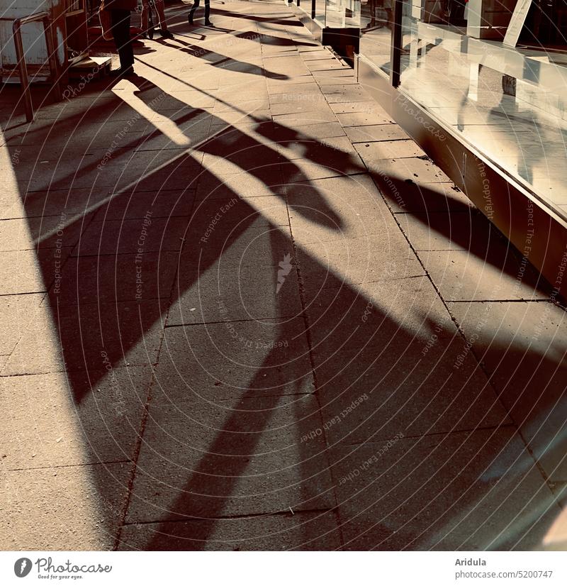 Licht und Schatten auf dem Fußweg vor der Ladenzeile Gehweg Einkaufszeile Läden Bürgersteig Steinplatten Personen Lichtspiel Schattenspiel Gegenlicht warm
