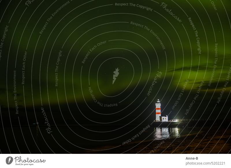 Kleiner Leuchtturm am Nordatlantik nachts, angestrahlt und mit einem wunderschönen Nordlicht am Himmel. Leuchtfeuer Sicherheit Altlantik Meer Island